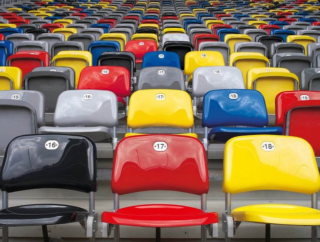 Bunte Sitze in der MERKUR SPIEL-ARENA. Die Sitze haben die Farben schwarz, rot, blau, gelb und grau. 